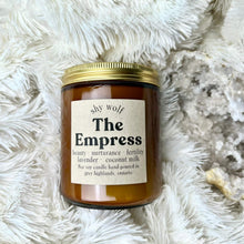 A clear soy candle with a label that reads 'The Empress' placed on a white furry surface, with a background that includes a small crystal.