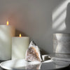 Candle holders with candles and a decorative stone on a white surface against a gray wall.