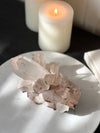 Pink Himalayan Quartz Cluster on white stand with book and candles.