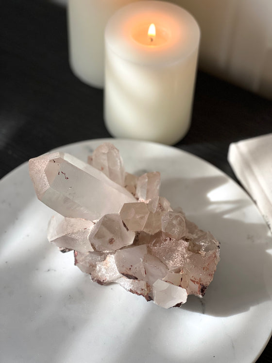 Pink Himalayan Quartz Cluster on white stand with book and candles.