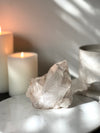 Pink Himalayan Samadhi Quartz on a marble stand with candles and a book in the background.
