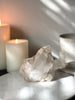 Pink Himalayan Samadhi Quartz on a marble stand with candles and a book in the background.