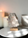 Pink Himalayan Samadhi Quartz on a wooden and silver stand with a blurred background featuring candles and a book.