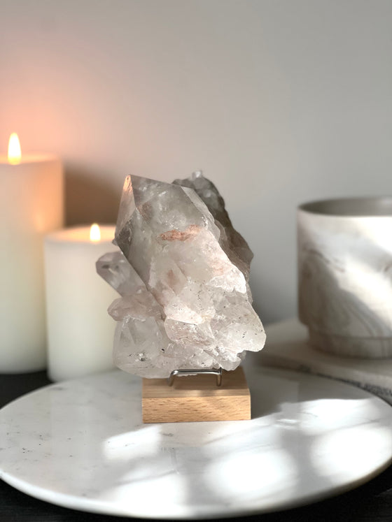 Pink Himalayan Samadhi Quartz on a wooden and silver stand with a blurred background featuring candles and a book.