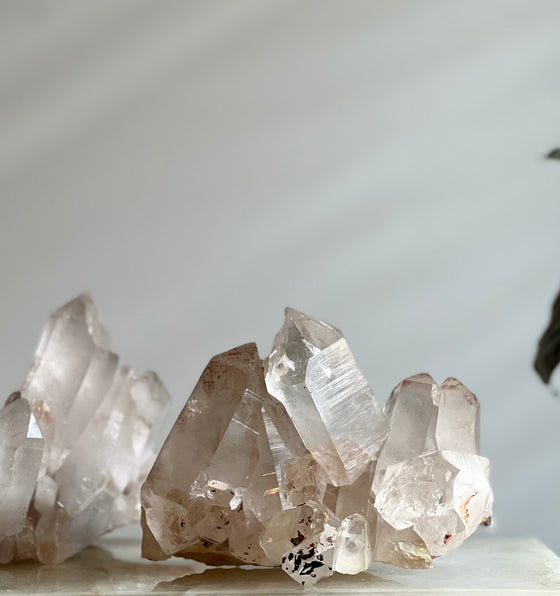 Pink Himalayan Samadhi Quartz on a white marble pedestal with candles and a book in the background.